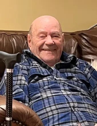 Passing of Robert Kuhn image of him wearing a plaid blue shirt with a smile on his face.