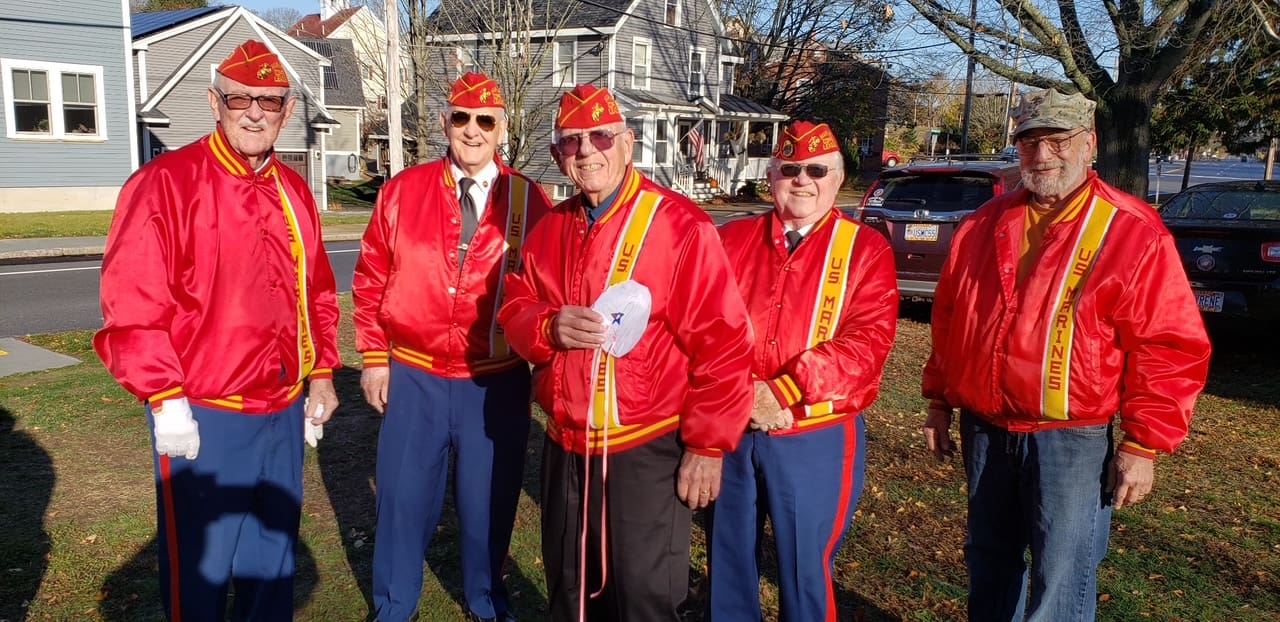 5 older men stand line wearing red silk jackets and red covers.